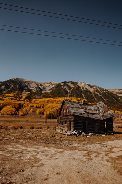 棕色的木屋在棕色的田野上，靠近棕色的山脉，白天在蓝天下